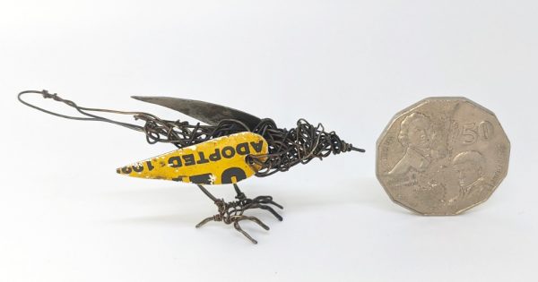 Wire sculpture of bird next to fifty cent coin